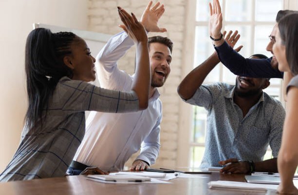 Multiracial euphoric business team people give high five at office table, happy excited diverse work group engaged in teambuilding celebrate corporate success win partnership power teamwork concept